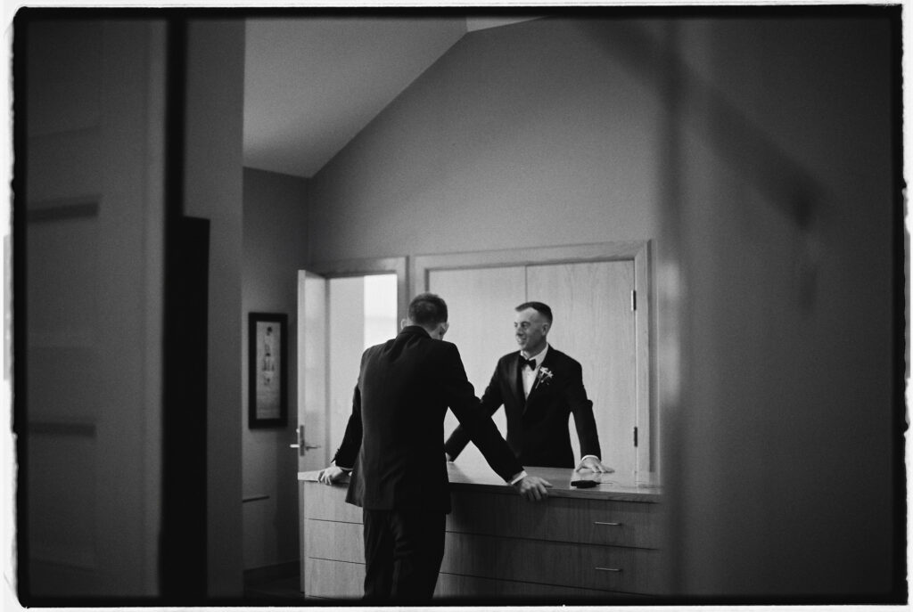 A photo photographed on film of the groom and his brother through a doorway before their church ceremony by Vermont and New England wedding photographer, Gold Wing Photography, specializing in authentic, cinematic, and candid moments.